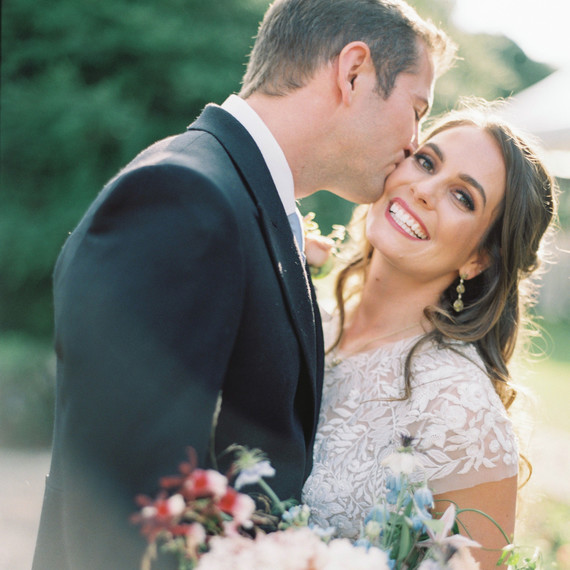 groom kissing bride on cheek outside smiling groom kissing bride on cheek outside smiling