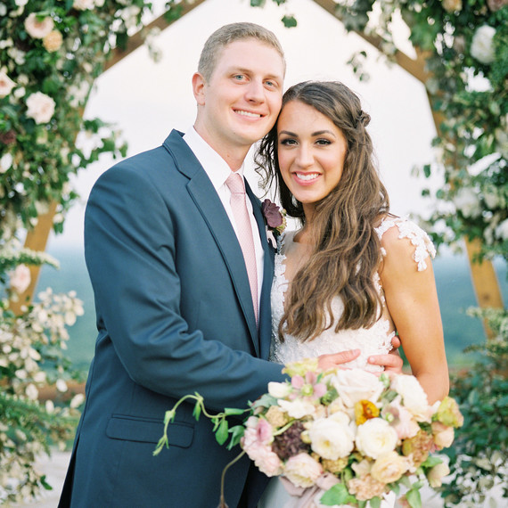 happy wedding couple pose under floral archway happy wedding couple pose under floral archway