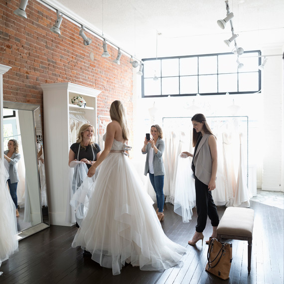 Woman Trying on Wedding Dress at Bridal Salon with Friends Woman Trying on Wedding Dress at Bridal Salon with Friends